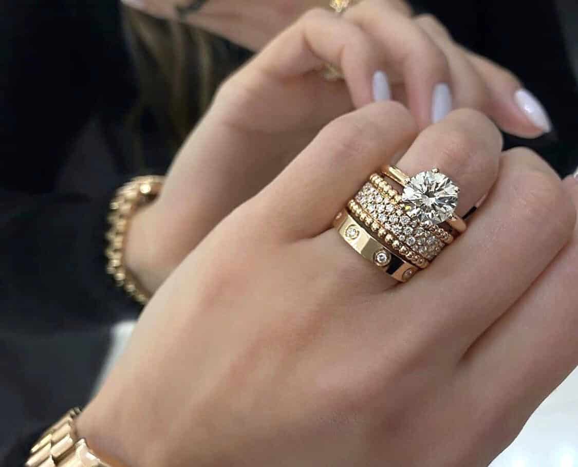 Duas alianças e um anel solitário em ouro amarelo na mão de uma mulher usando relógio