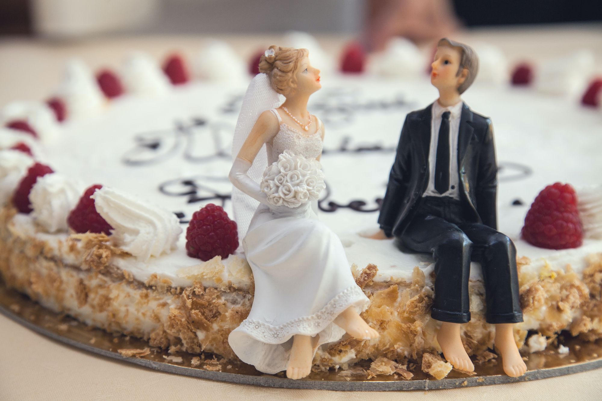 Foto colorida de bonecos sentados em cima do bolo de casamento.