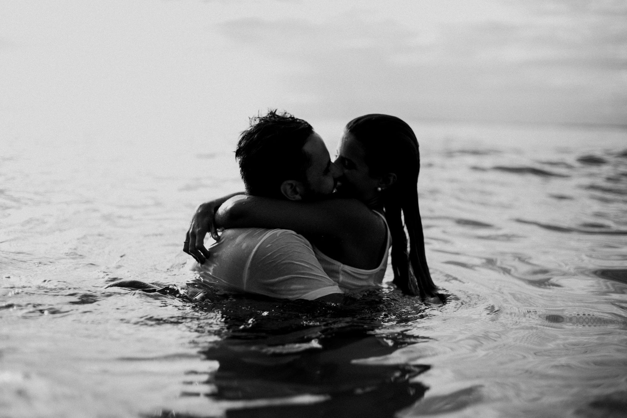 Foto preto e branco de casal se beijando dentro do mar.