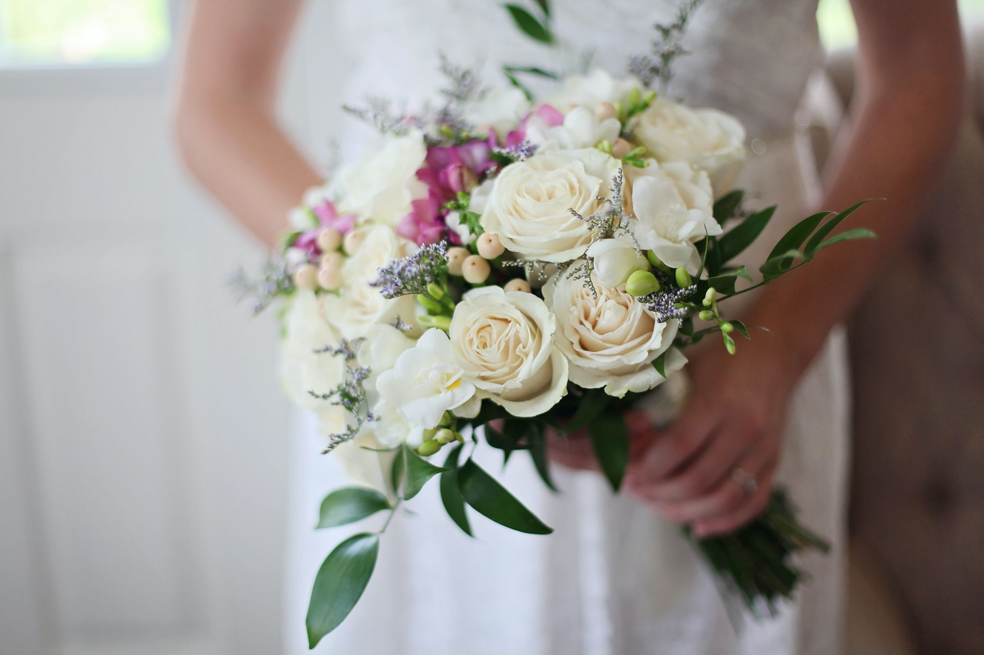 Foto colorida de mulher vestida de noiva segurando buquê de flores brancas.
