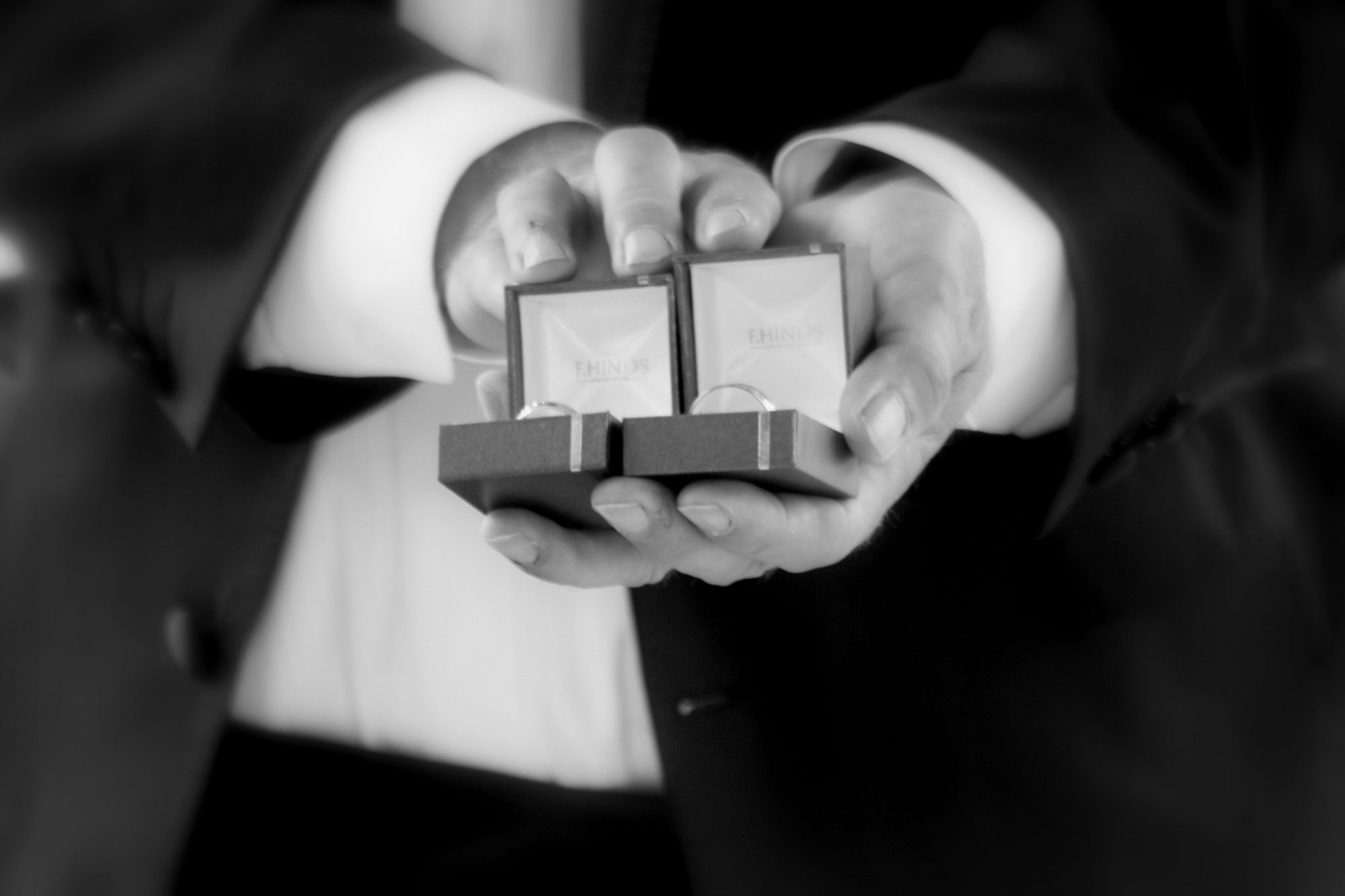 Foto preto e branco de noivo segurando as caixas abertas das alianças.