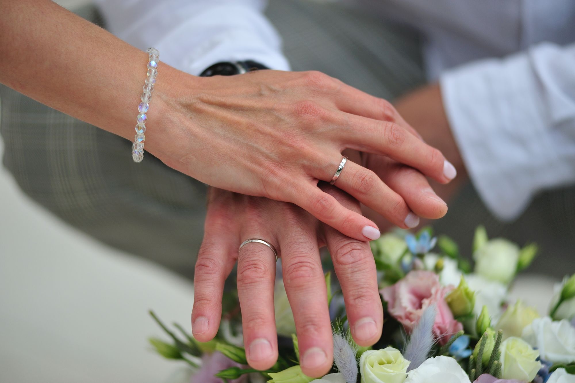 Foto colorida de noivos cruzando as mãos sobre buquê de flores.