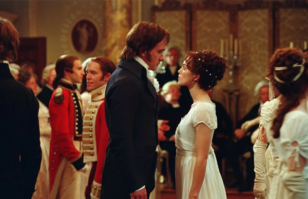 Foto colorida dos personagens elizabeth e mr. Darcy olhando um para o outro em meio ao salão de dança.
