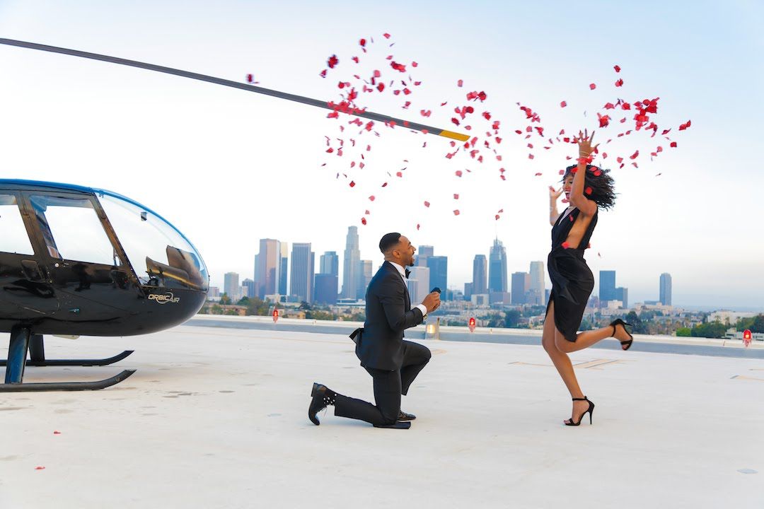 Homem pedindo sua noiva em casamento, após um passeio de helicóptero, e com uma chuva de pétalas de rosas
