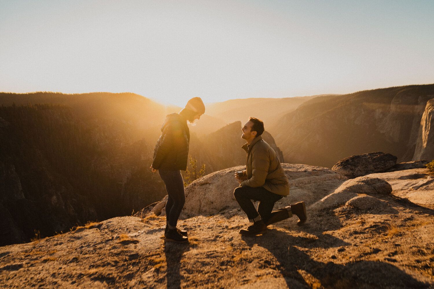 Homem pedindo sua noiva em casamento, durante uma viagem, em frente às montanhas