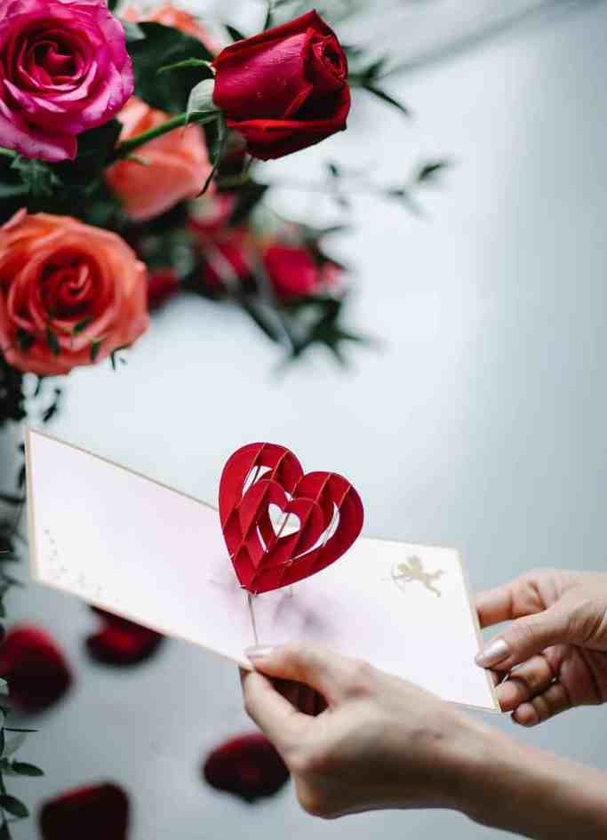 Carta de amor aberta tem um coração em alto relevo, atrás tem um buquê de rosas.