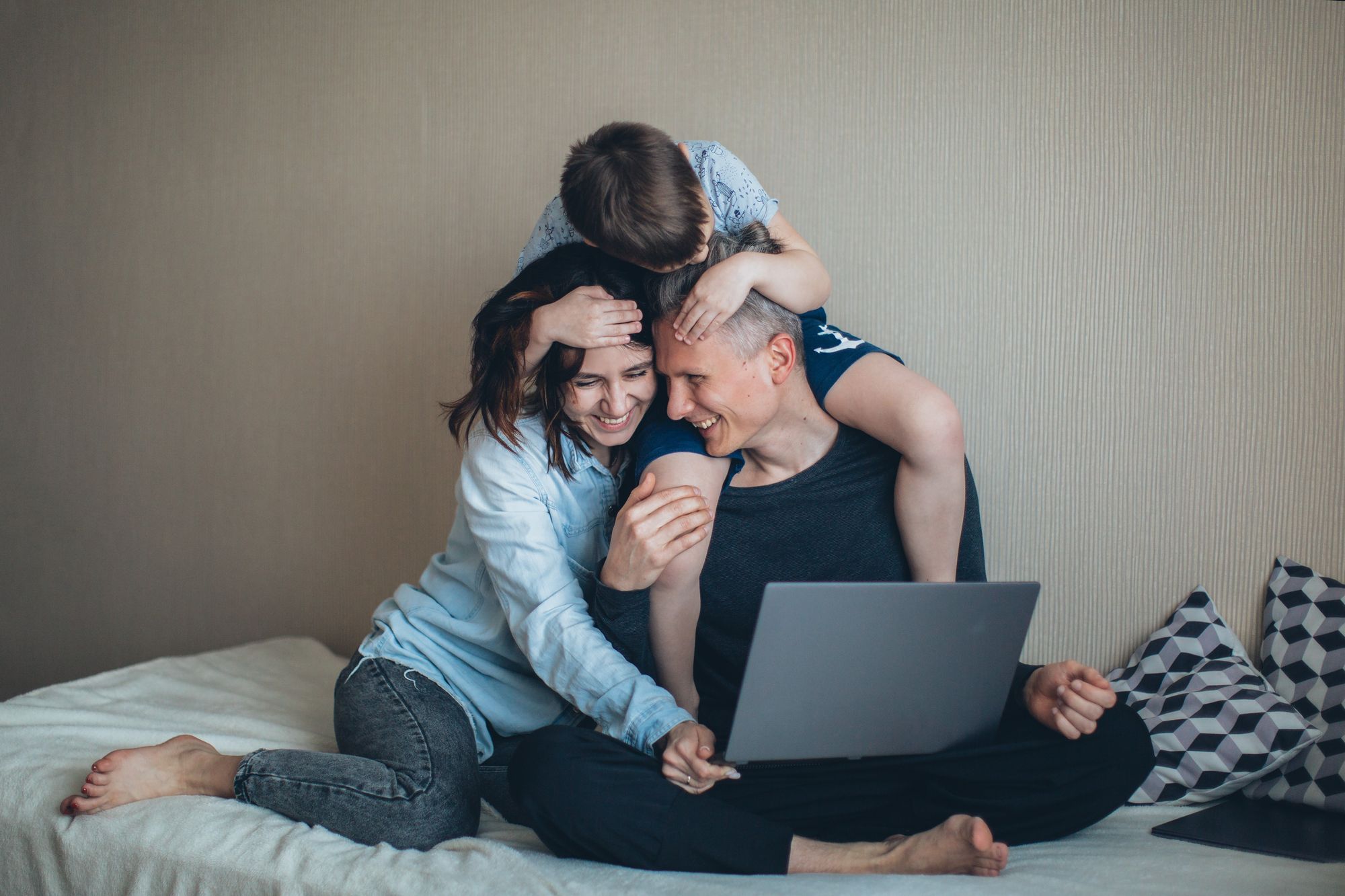 Foto de casal com o filho sentados na cama. Eles estão sorrindo.