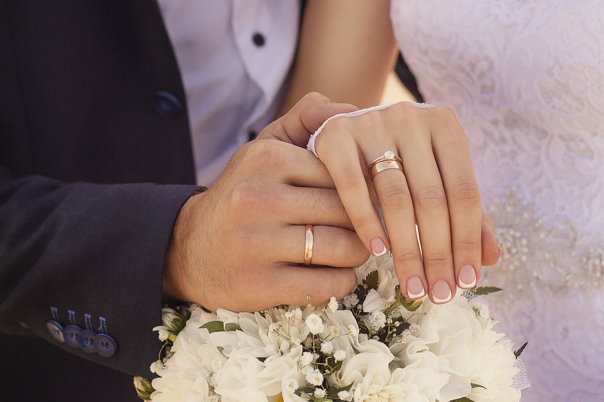 Foto de recém casados segurando as mãos e mostrando as alianças de casamento.