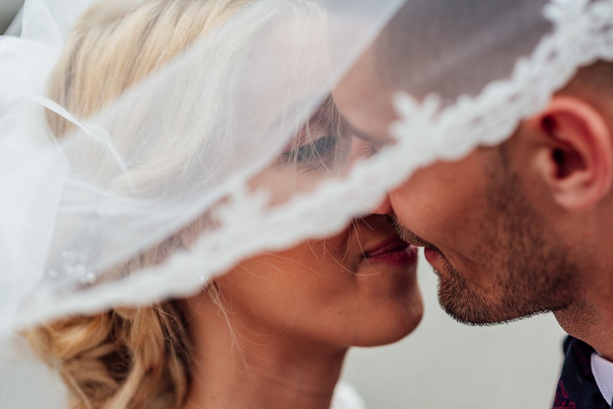 Foto de casal recém-casado se beijando embaixo do véu da noiva.