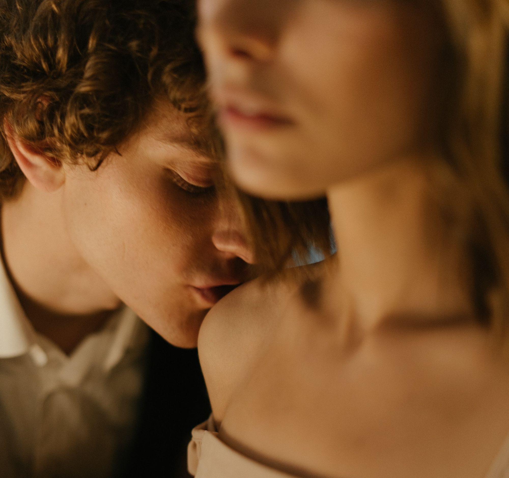 Foto colorida de homem beijando o ombro da mulher amada.
