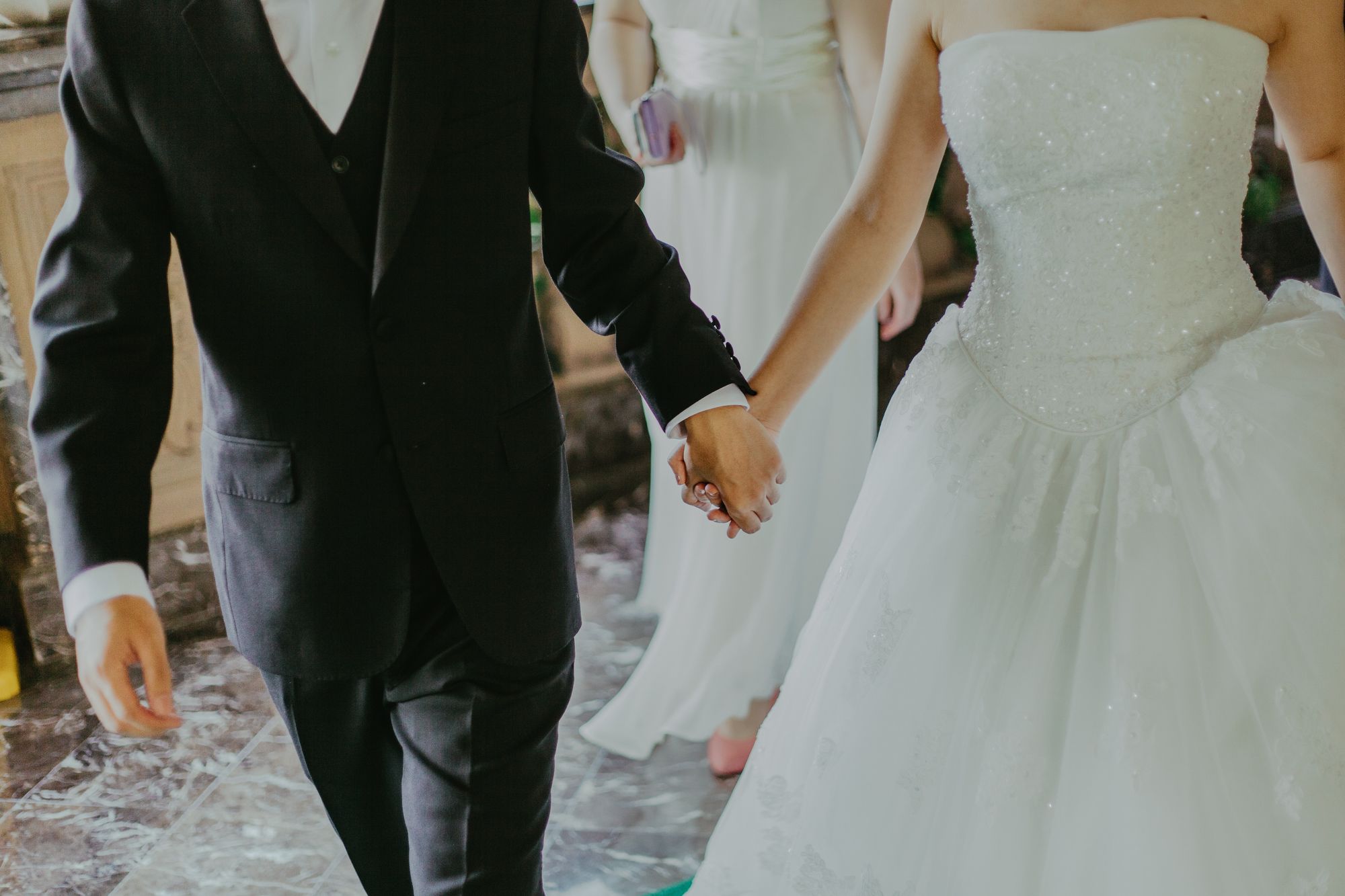 Foto colorida de casal recém-casado saindo de mãos dadas da cerimônia de casamento.