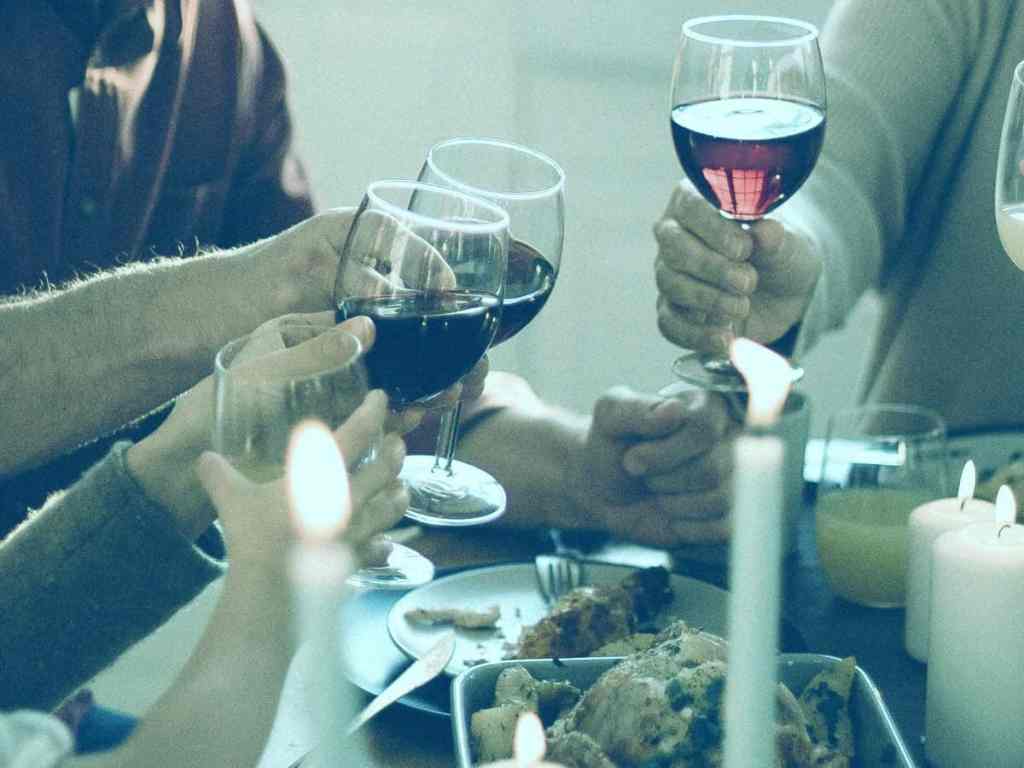 A imagem está cortada de forma que só pode se ver parte da mesa com pratos de comida, e as pessoas brindando com taças de vinho.