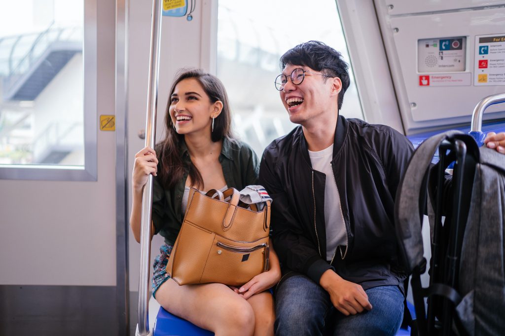 Foto de casal sentado em banco de metrô. Eles estão sorrindo.