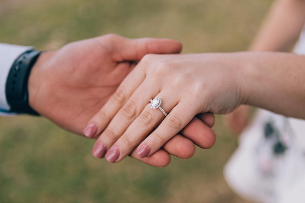 Foto do noivo segurando a mão da mulher. Ela usa um anel de noivado