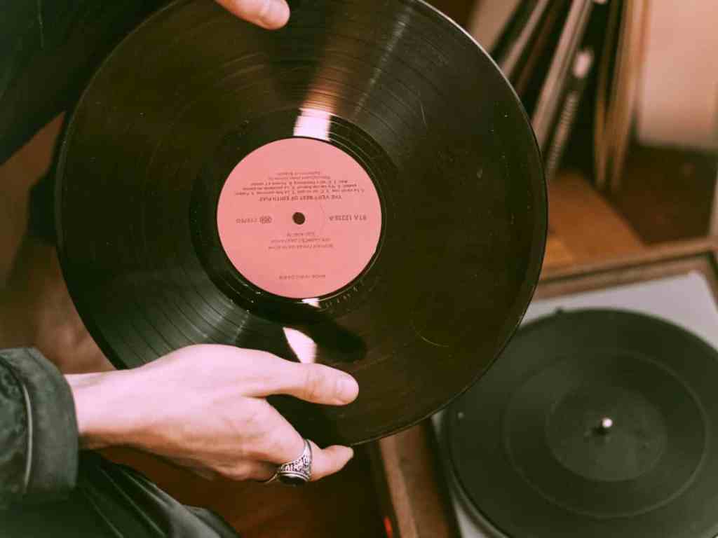 Pessoa colocando disco de vinil na vitrola, em que a caixa é marrom.