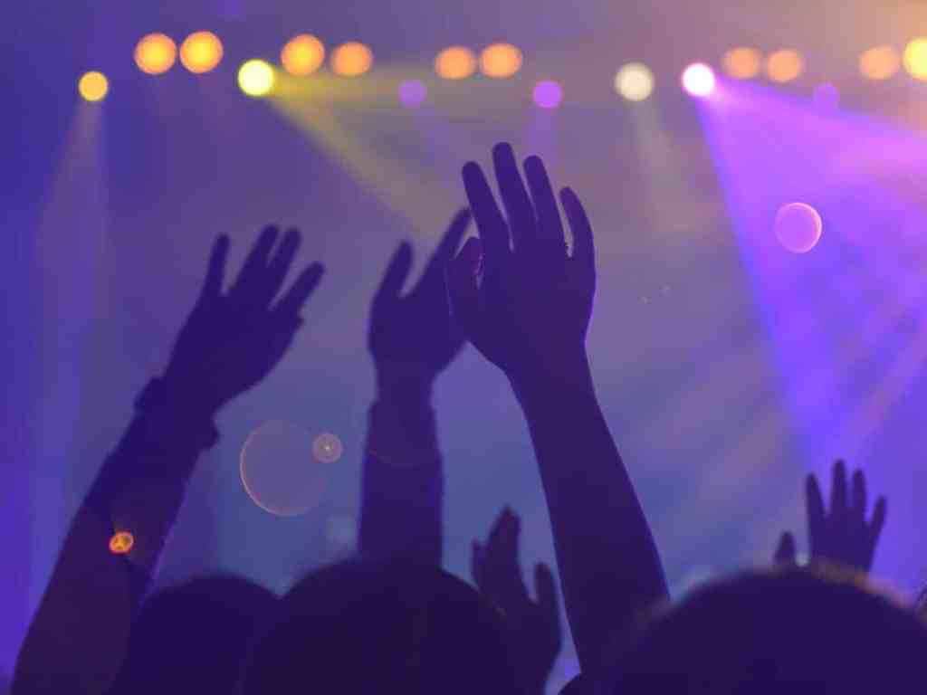 Mãos levantadas curtindo um show, várias luzes amarelas na frente.