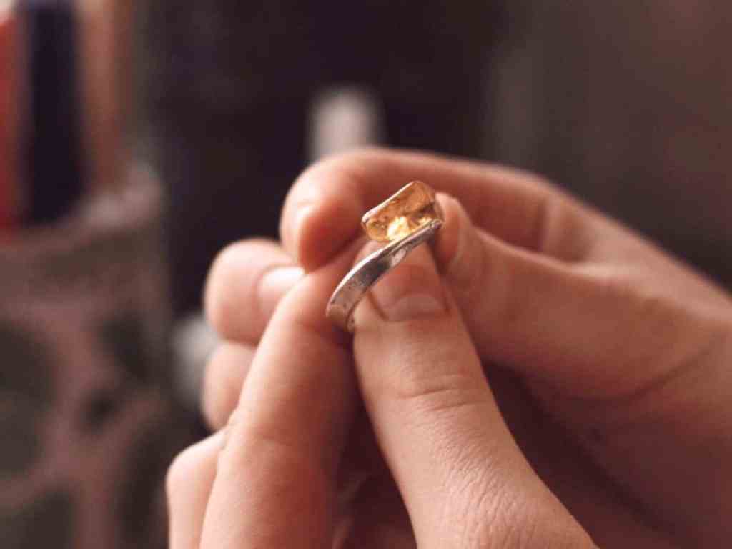 Segurando um anel na cor prata com pedra amarela.