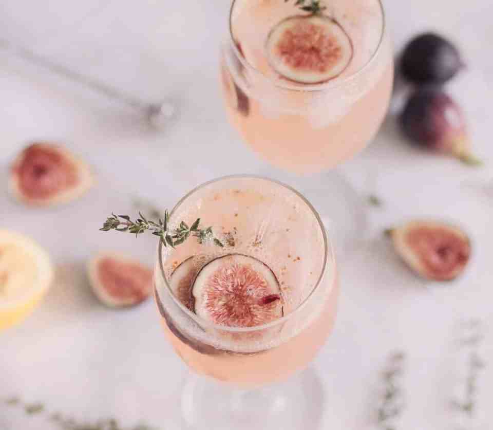 Imagem de dois cocktails na cor pêssego, na mesa tem algumas frutas pequenas espalhadas. Este é um exemplo de bebidas perfeitas para casamento.