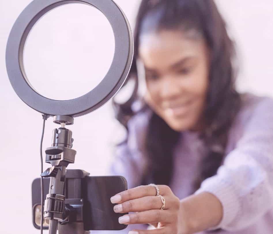 Garota com rabo de cavalo segurando o microfone do podcast. Ela veste suéter lilás e usa vários anéis no dedo.