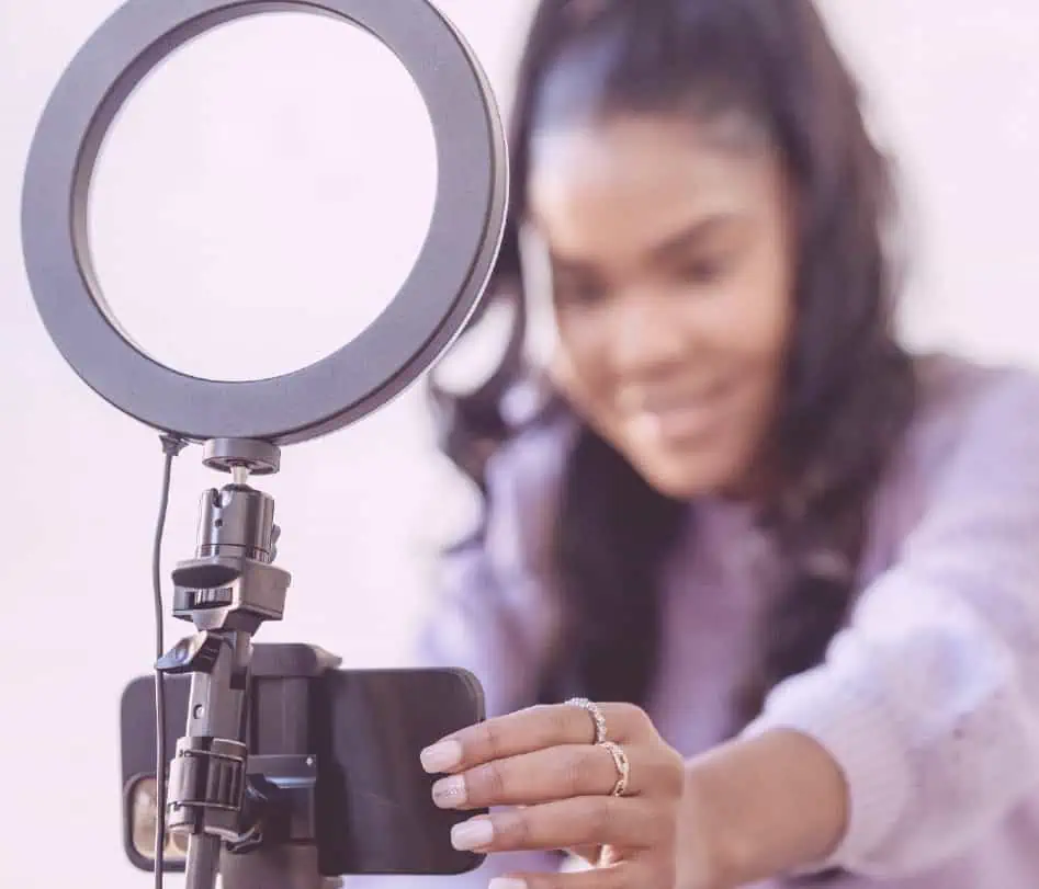 Garota com rabo de cavalo segurando o microfone do podcast. Ela veste suéter lilás e usa vários anéis no dedo.