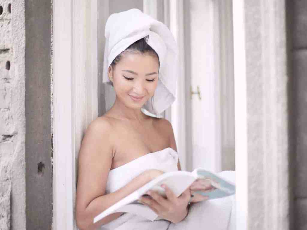 Mulher de toalha no corpo e no cabelo lendo uma revista.