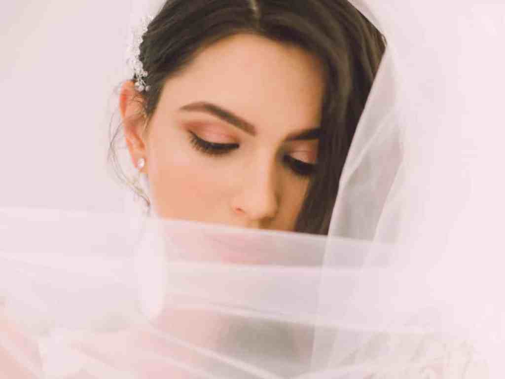 Noiva de olhos fechados com véu longo branco.