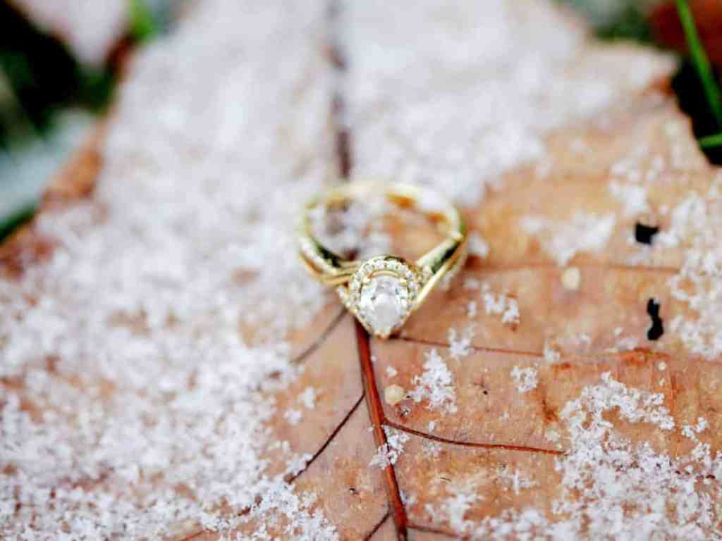 Aliança de ouro com pedra em cima de uma folha cheia de neve.
