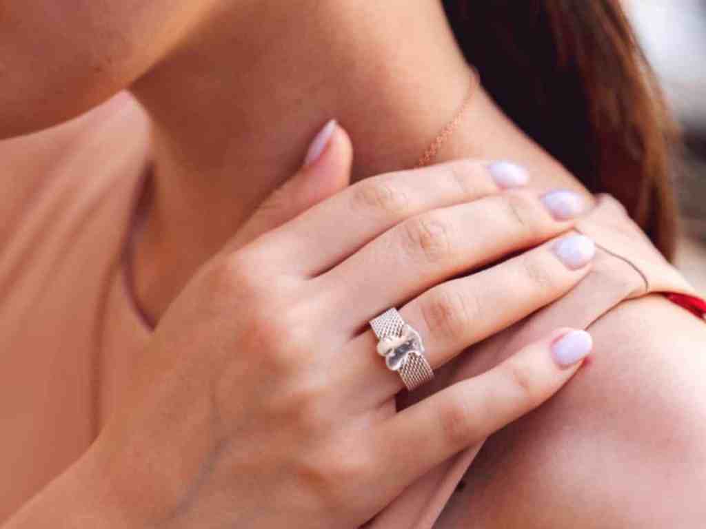 Inspiração: unhas de noiva delicadas - Anel-prata-unhas-de-noivas Mulher com a mão no ombro, mostrando o anel prata e as unhas brancas.