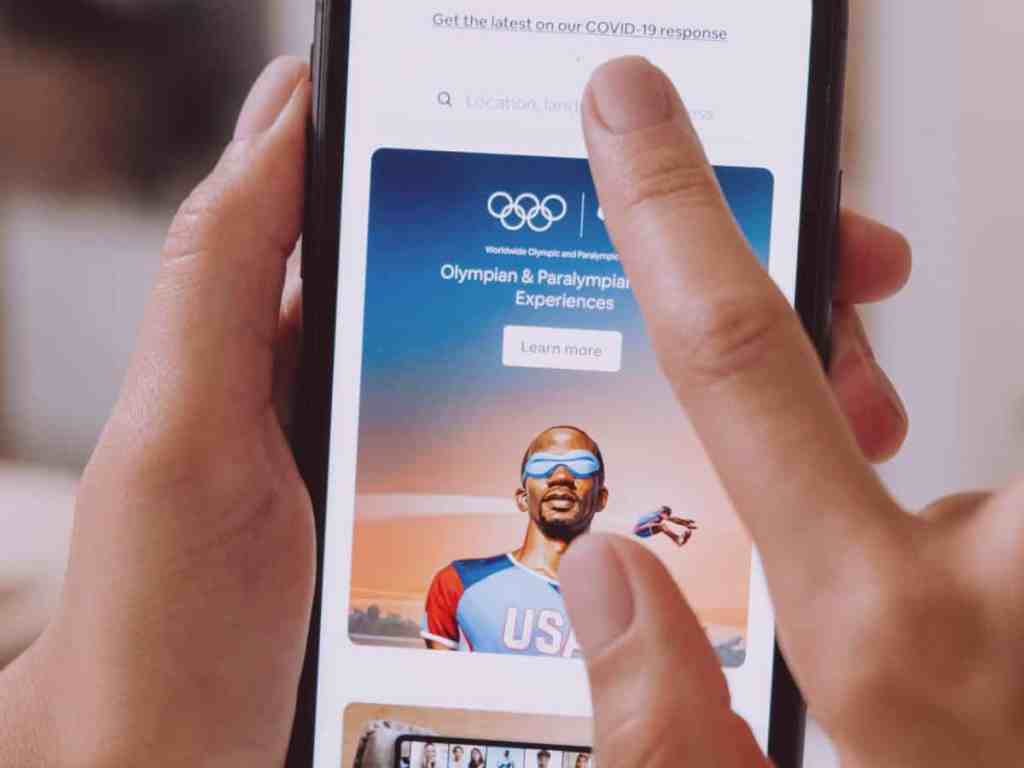 Pessoa mexendo no celular, tem um anúncio das olimpíadas na tela.