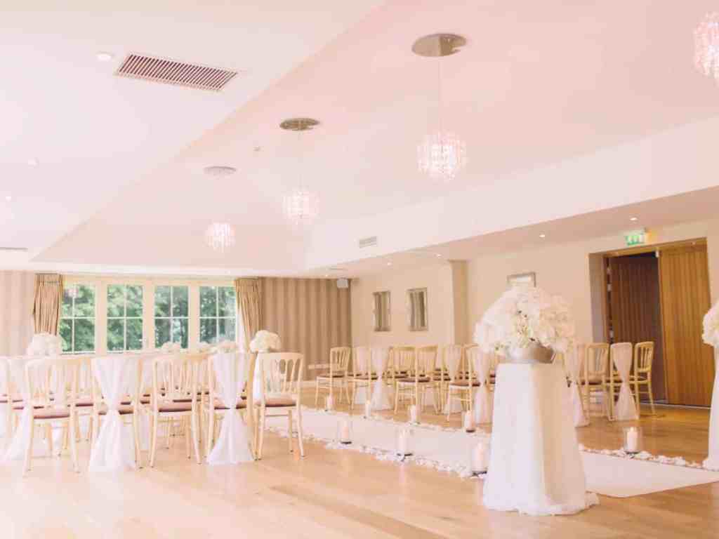 Qual é a melhor cor para decoração de casamento? - Decoracao-de-casamento-claro-branco-fechado-salao Decoração de casamento branca com detalhes dourados. É um espaço fechado com mesas e cadeiras e buquês.