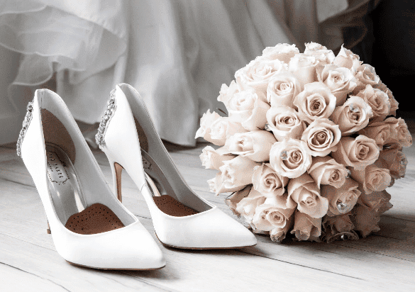 Buquê e sapato da noiva no chã, atrás pode se ver o vestido.