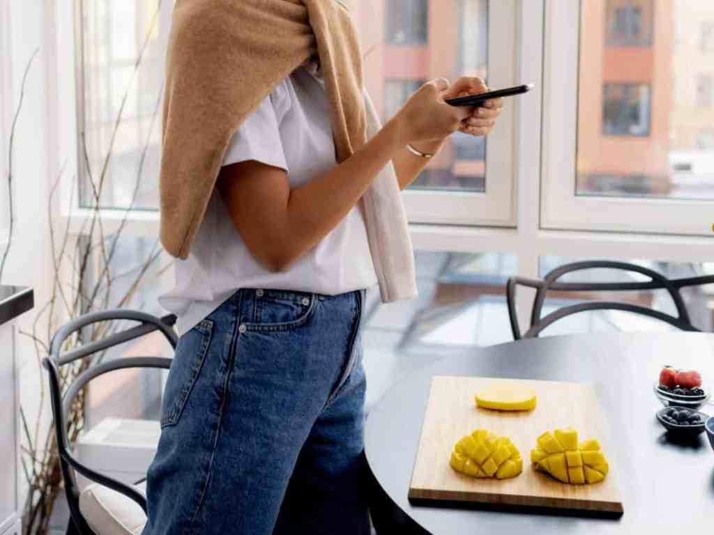 Mulher em pé tirando foto com o celular de uma fruta picada.