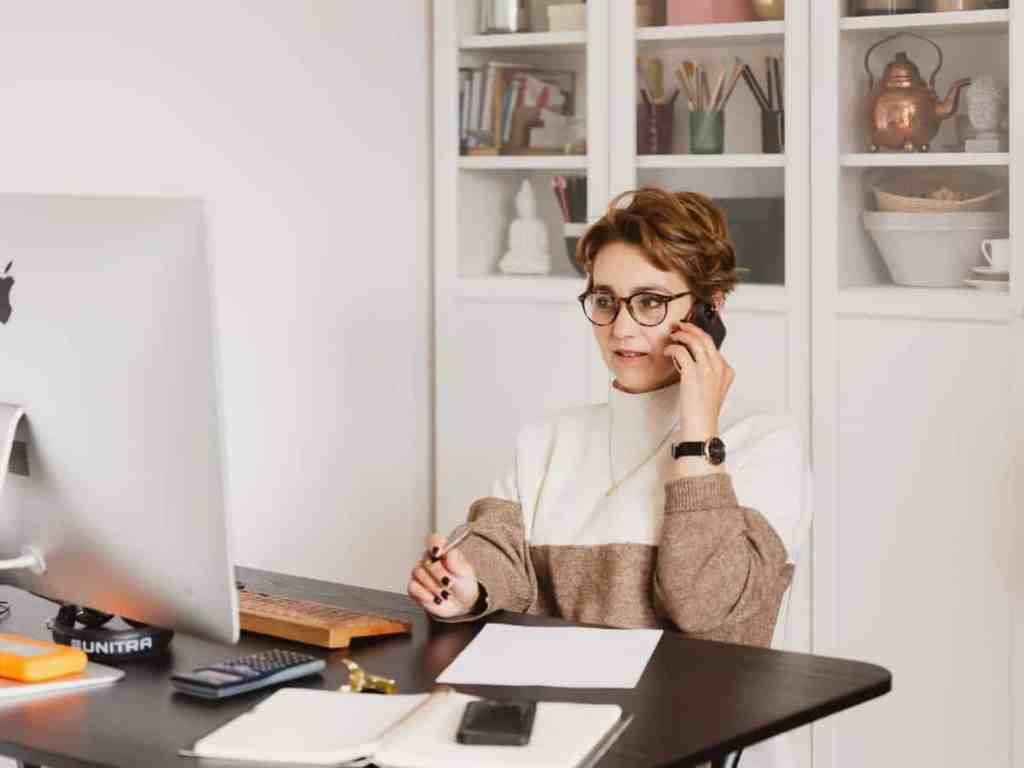 Mulher de cabelo curto e óculos falando no telefone enquanto está de home office.