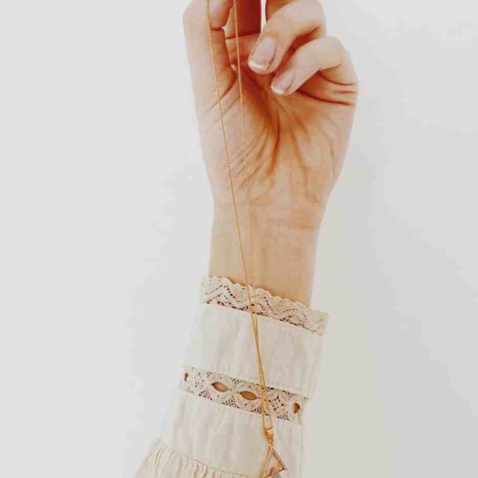 Como limpar joias e semijoias? - Colar-dourado-pingente Segurando a corrente do colar dourado.