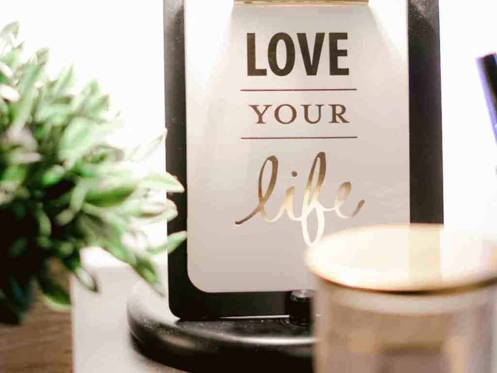 Quadro em cima da mesa escrito "love your life" (ame sua vida).