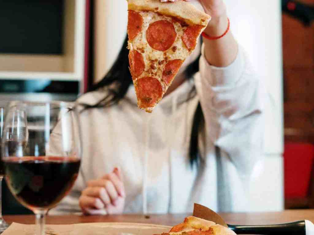 Garota segurando pedaço de pizza na frente do rosto.