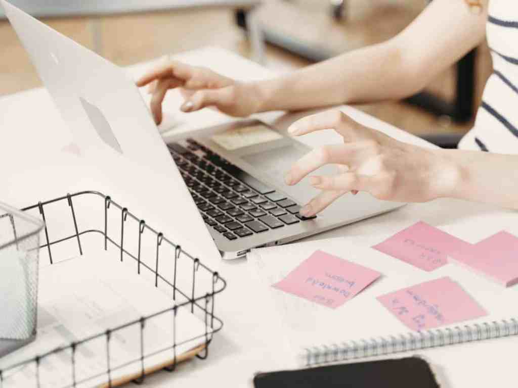 Cursos on-line gratuitos de empreendedorismo - Planejar-post-it-notebook Digitando no notebook, do lado tem um caderno com vários post-its pregados.