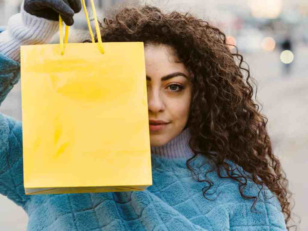 Mulher segurando sacola de compras amarela em frente ao rosto.
