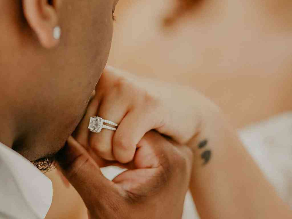 Homem beijando mão da noiva que usa anel solitário.