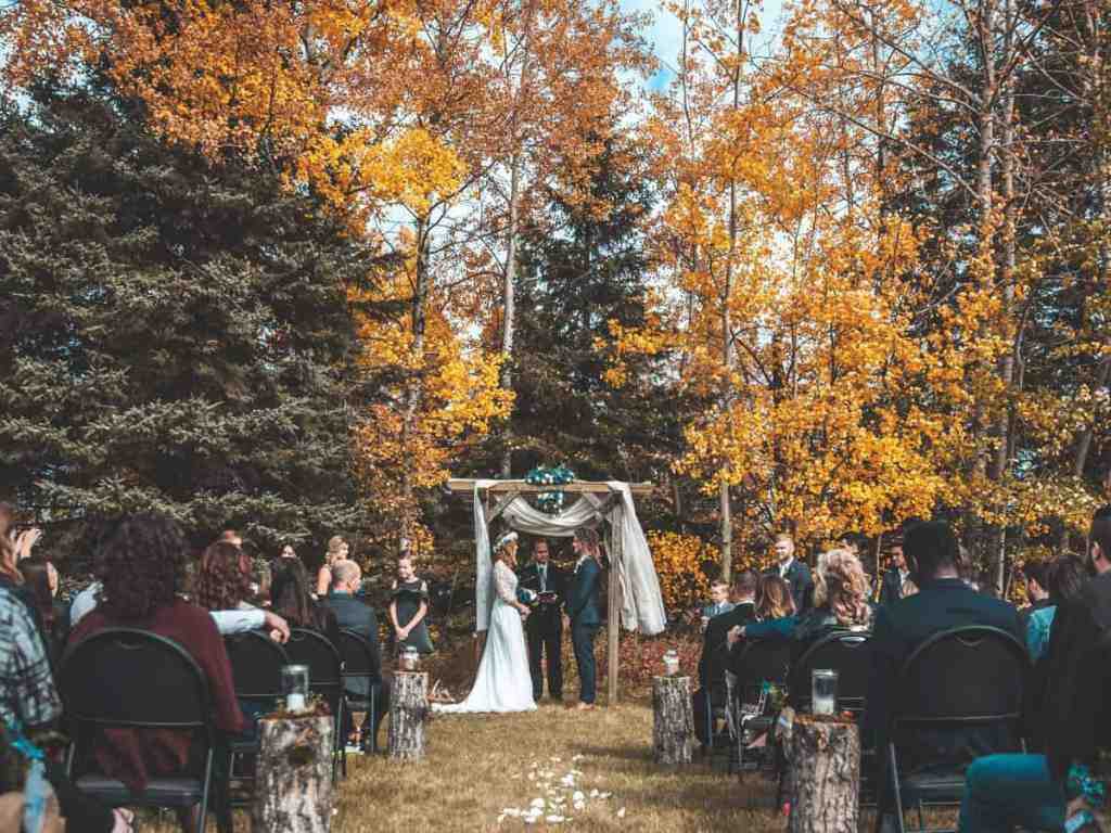 Noivos se casando ao ar livre, convidados sentados nas cadeiras assistindo.