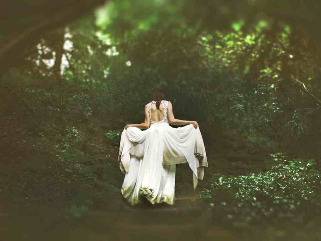 Noiva andando na floresta, segurando a barra do vestido