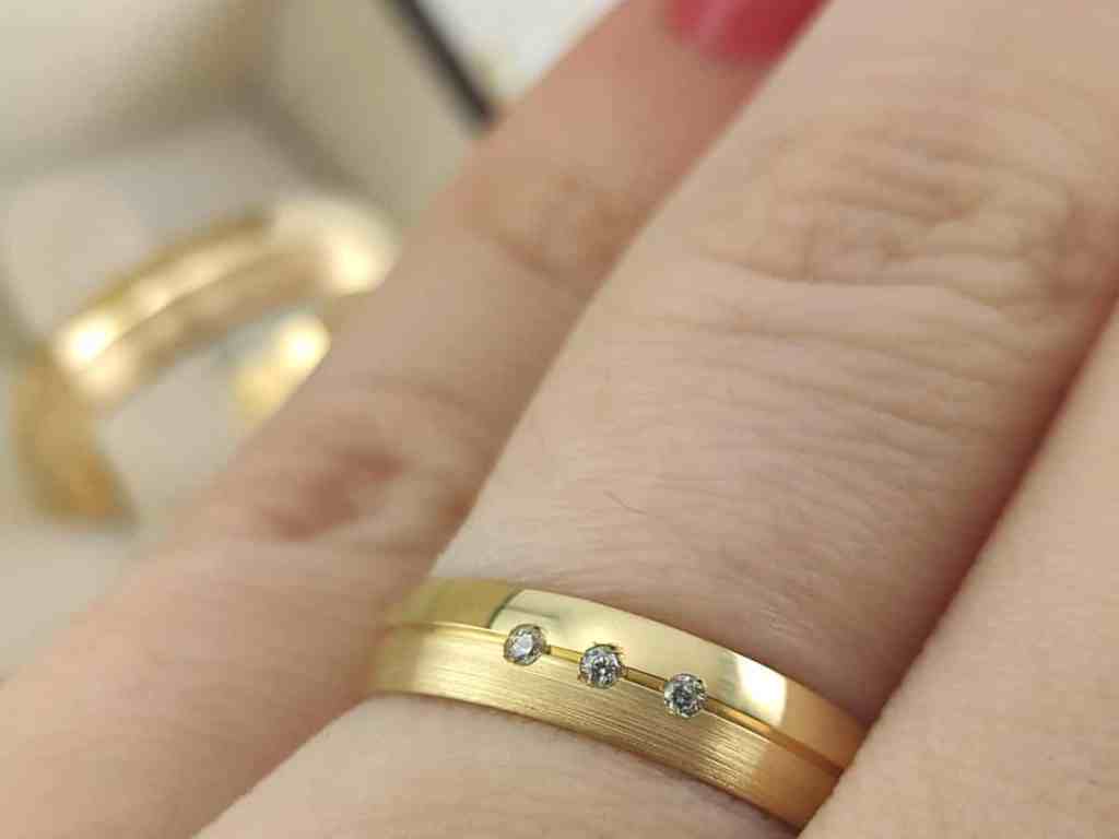 Guia Definitivo das Pedras: Tipos de Cravação e Lapidação - Alianca-cravacao-bigodinho Par de alianças de ouro amarelo. Anel com 3 pedras e risco no meio.