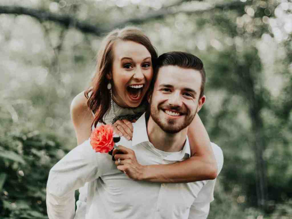 6 hábitos que todos casais felizes têm juntos - Casal-feliz-saudavel Mulher abraçada nas costas do namorado, segurando uma flor. Ambos estão felizes