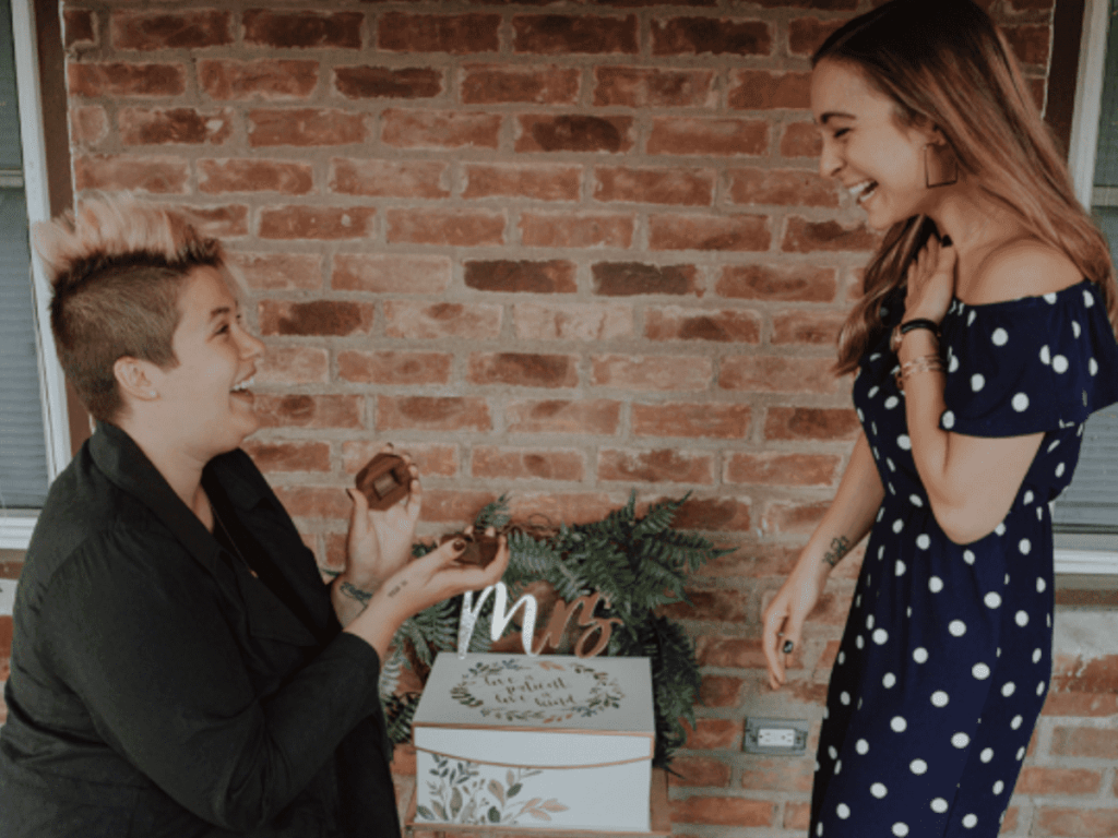 Mulher ajoelhada pedindo sua namorada em casamento.