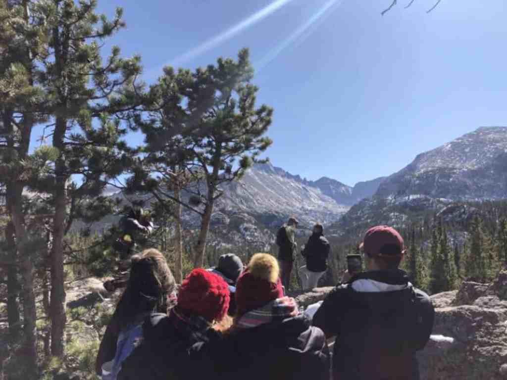 Grupo de pessoas usando jaquetas de frio assistindo pedido de casamento no topo da montanha.