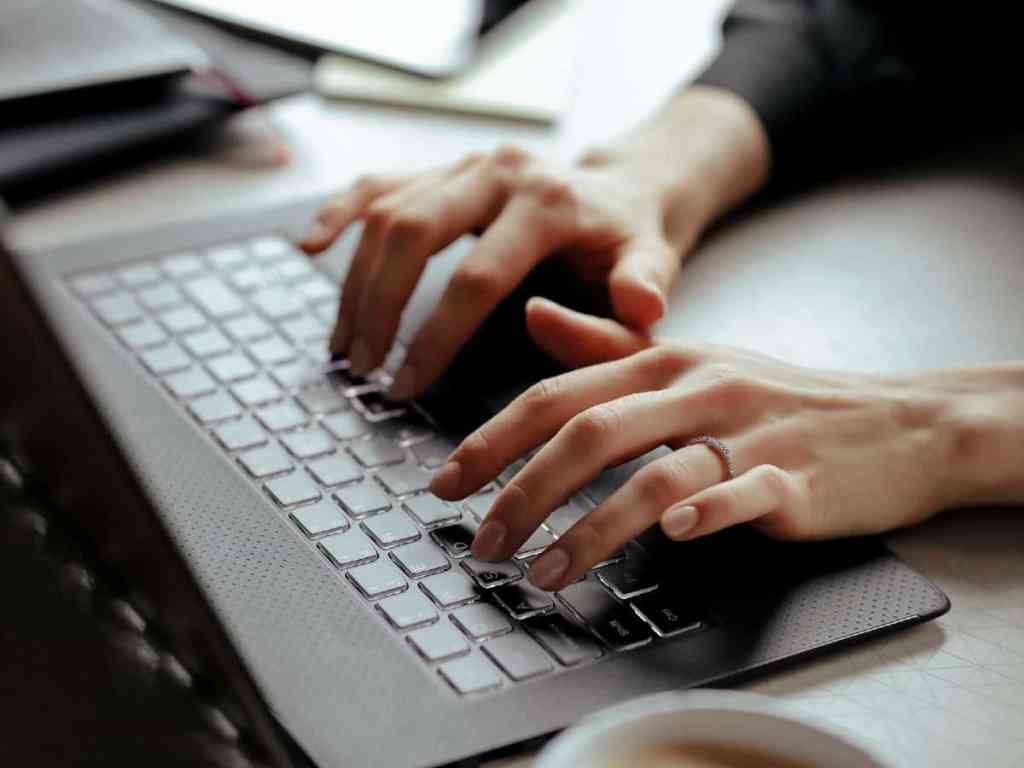 Mãos femininas digitando no teclado do notebook, usa aliança