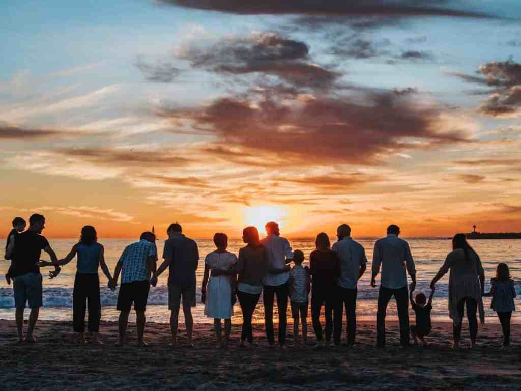 Família grande de mãos dadas assistindo o pôr do sol na praia.
