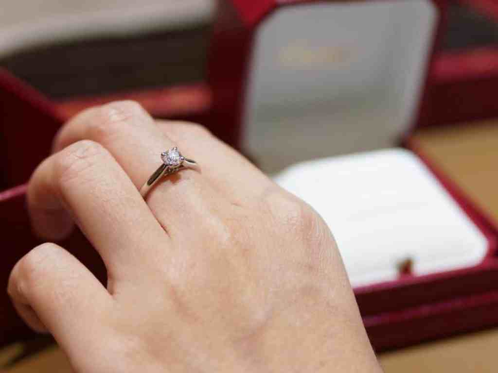 Mão usando anel solitário com caixinha vermelha no fundo