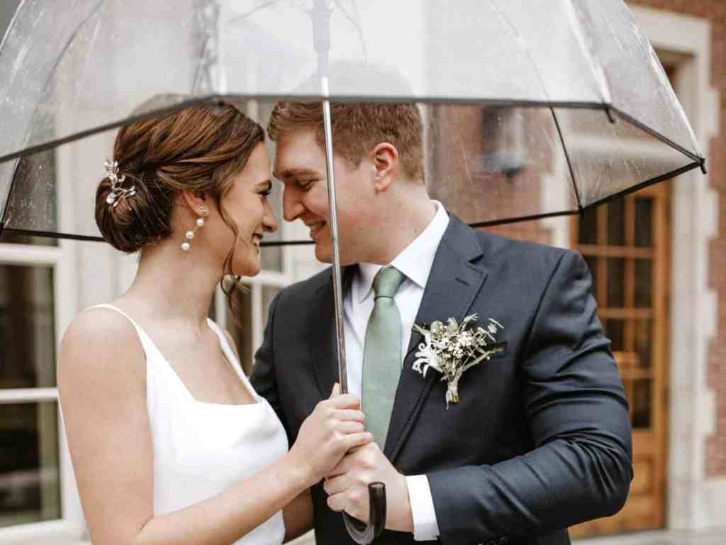 Noivos felizes debaixo de um guarda-chuva transparente