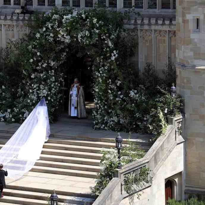 Meghan markle subindo as escadas da igreja para se casar, com véu de longa calda.